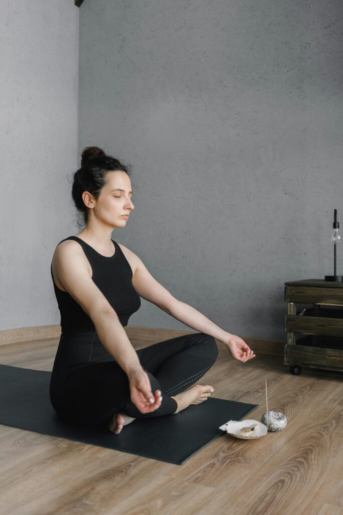 Home A woman in a serene pose meditates indoors, surrounded by candles and incense, symbolizing relaxation.